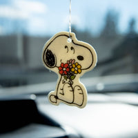 Car air freshener shaped like a cartoon dog holding flowers, hanging from a car's rearview mirror.