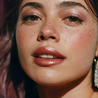 Close-up of a woman with freckles and pink makeup, wearing a large earring.