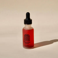 Bottle of red liquid with a dropper on a beige background