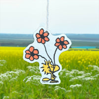 Car air freshener with cartoon character and flowers hanging in a field