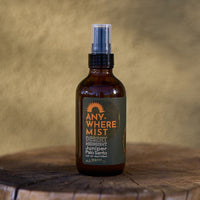 Brown spray bottle labeled 'Anywhere Mist' on a wooden surface with a brown background