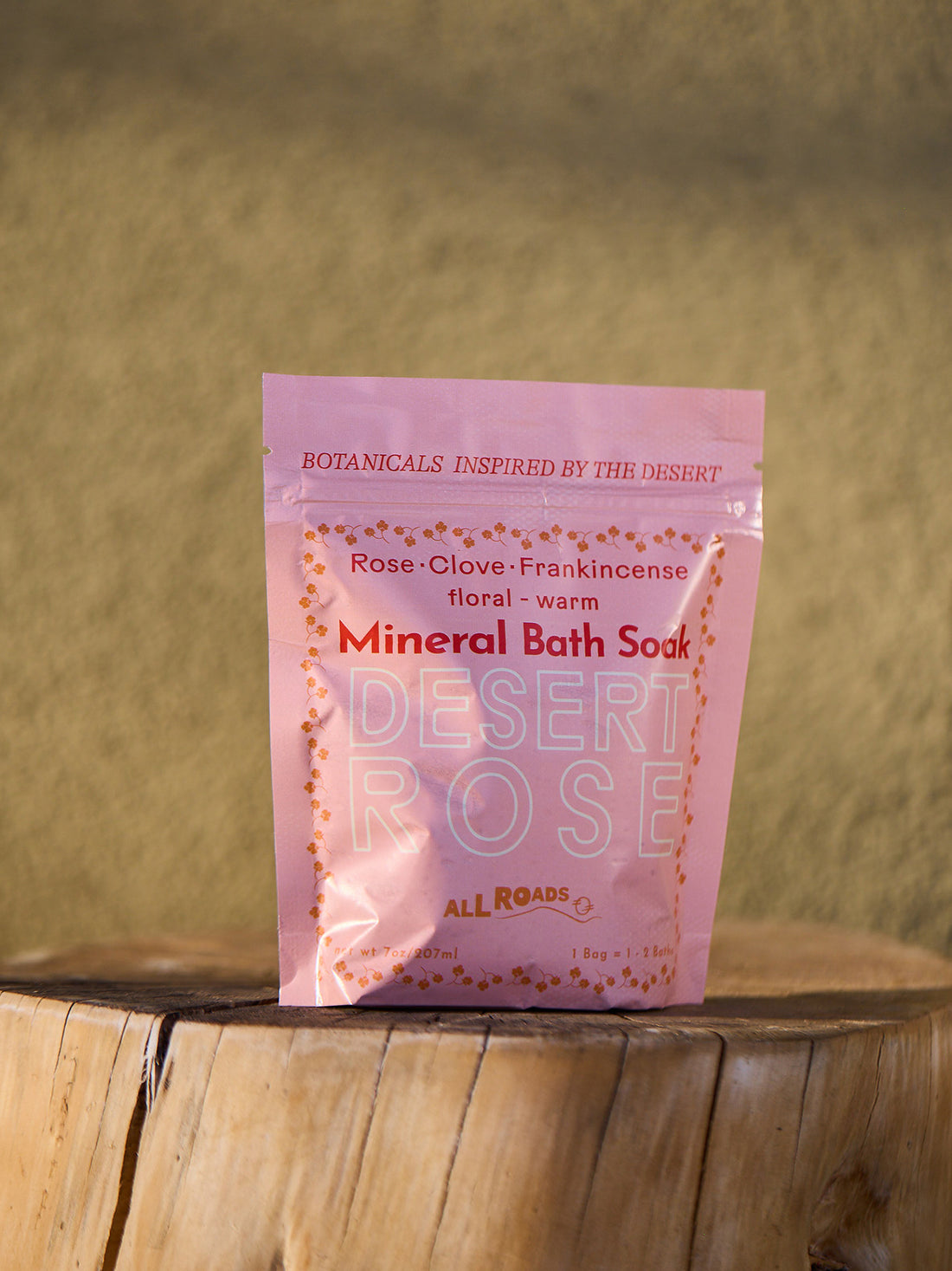 Pink package of Desert Rose Mineral Bath Soak on a wooden surface with a blurred natural background