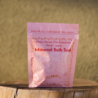 Pink package of Desert Rose Mineral Bath Soak on a wooden surface with a blurred natural background