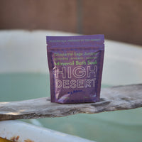 Purple packet of High Desert Mineral Bath Soak on a wooden surface with a blurred background