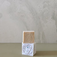 Bar of soap on a white cube with a label against a textured light gray background