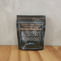 A green pouch of mineral bath salts containing palo santo and juniper essential oils.