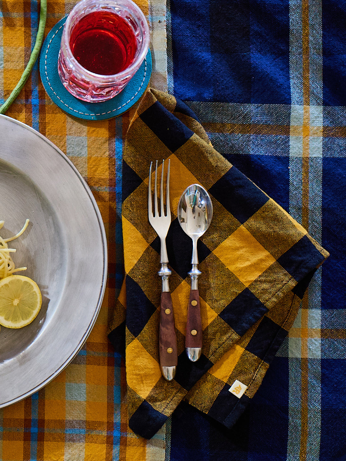 Table setting with a plaid tablecloth, silverware, and a glass of red wine.