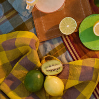 Fruits on a checkered tablecloth with colorful coasters and a drink.