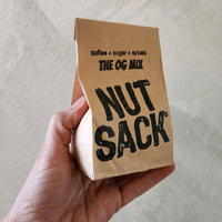 Hand holding a 'Nut Sack' package with text on a neutral background