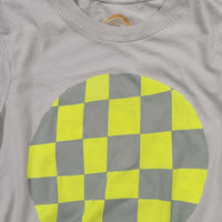 A close-up of a light sage green crewneck t-shirt featuring a large circular graphic on the front with a yellow and gray checkerboard pattern.