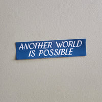 Blue sticker with 'Another World is Possible' text on a gray background