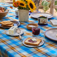 Outdoor breakfast table with plaid tablecloth, sunflowers, and food items.