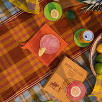 Colorful picnic setup with drinks, snacks, and a book on a checkered blanket.