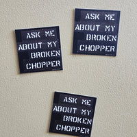 Three stickers with 'Ask me about my broken chopper' text on a light gray wall.