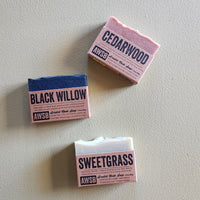 Three bars of soap with labels 'Black Willow', 'Cedarwood', and 'Sweetgrass' on a light gray background.