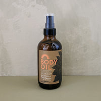 A bottle of Desert Midnight body oil with a spray nozzle, featuring a label with desert-inspired artwork.
