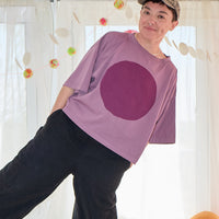 Person wearing a purple t-shirt with a large round design, standing in a room with decorative elements.