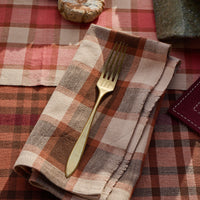 Folded plaid napkin with a gold fork on a red and brown checkered tablecloth.