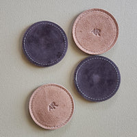 Four round leather coasters with 'AR' branding on a light gray background