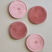 Four pink circular coasters with initials on a light gray background