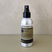 A silver spray bottle of 'Anywhere Mist' in the 'Desert Midnight' scent, standing on a beige surface against a textured beige wall.