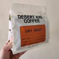 Desert Kid Coffee package labeled 'Dry Heat' held by a hand against a neutral background