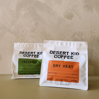 Two packages of Desert Kid Coffee on a beige surface with a beige background