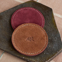 Two leather coasters, one brown and one purple , on a dark stone surface.