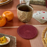 Table setting with a ceramic cup, coaster, and food items on a checkered tablecloth.