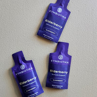 Three Gymbiotika Elderberry immune support packets on a light gray background