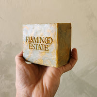 Hand holding a bar of soap with 'Flaming Estate' branding against a beige background