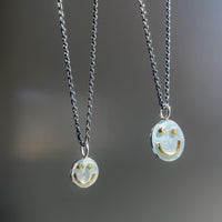 Two silver necklaces with smiley face pendants on a blurred gray background