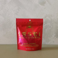 A red stand-up pouch of Issei Mochi Gummies, Sour Cherry flavor, standing on a beige surface against a textured light gray wall.
