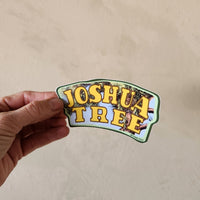Hand holding a 'Joshua Tree' sticker against a beige background