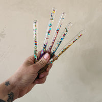 A hand holding a variety of small wands filled with multi colored glitter.