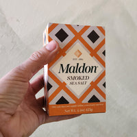 Hand holding a box of Maldon smoked sea salt against a light background
