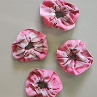 Four pink and white tie-dye scrunchies on a light gray background
