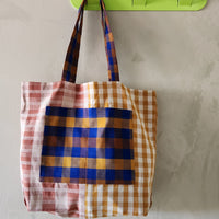 Plaid tote bag hanging on a green hook against a plain background