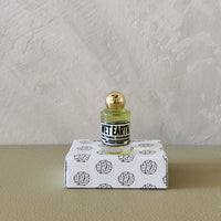 A small clear glass bottle with pale yellow liquid and a gold cap sits on top of a white box printed with black brain illustrations. The bottle label reads 'MET EARTH'.