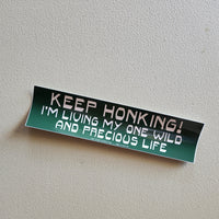A bumper sticker that reads "Keep honking! I'm living my one wild and precious life"