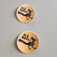 Two round stickers with a roadrunner graphic and 'All Roads' text on a gray background.