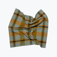 A napkin with a muted green and mustard yellow plaid pattern, styled in a loose knot against a plain white background.