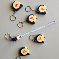 black and yellow mini tape measure with All Roads logo keychain.