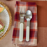 Silver fork and spoon on a purple and white checkered napkin with a plaid tablecloth.