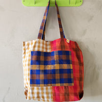 Colorful plaid bag hanging on a green hook against a light gray background