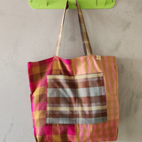 Colorful plaid bag hanging on a green hook against a plain wall.