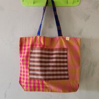Colorful checkered bag with a striped pocket hanging on a green hook against a plain wall.