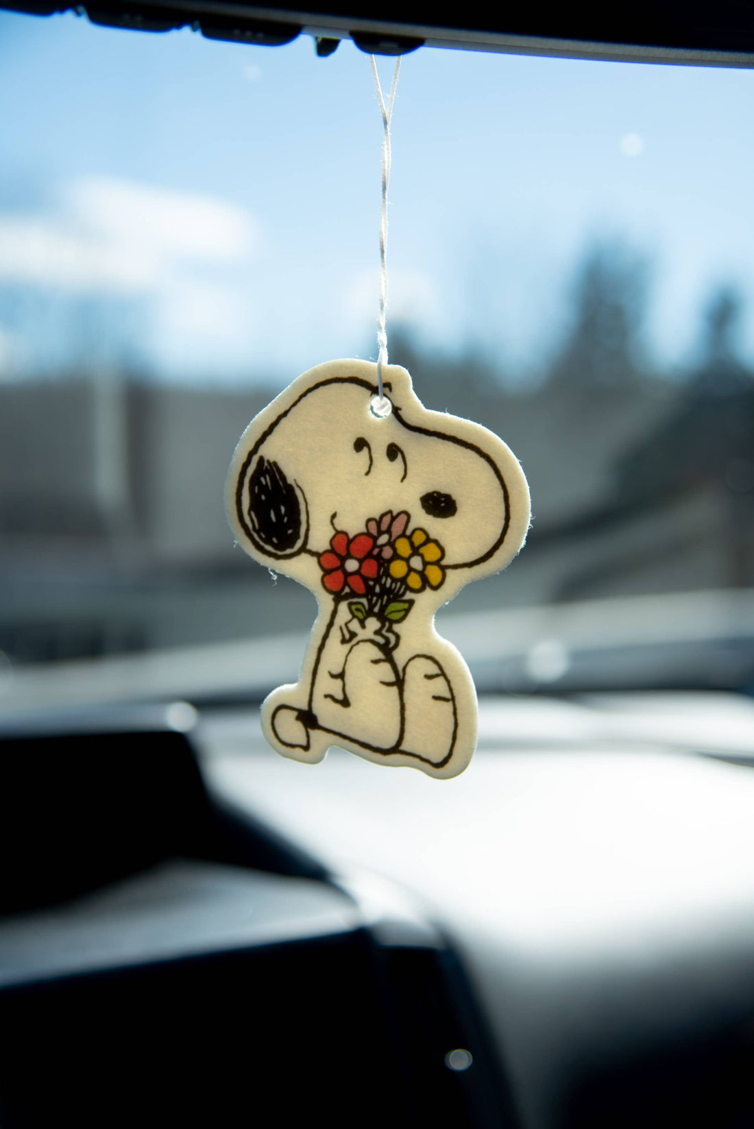 Car air freshener shaped like a cartoon dog holding flowers, hanging from a car&