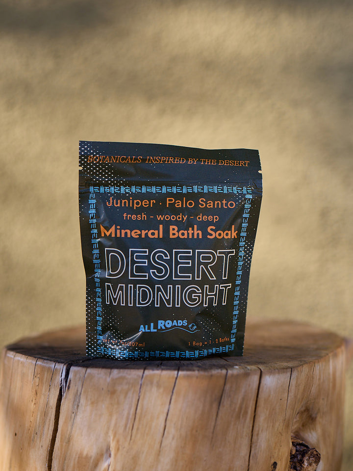 Mineral bath sock packaging labeled 'Desert Midnight' by All Roads on a wooden surface with a blurred background.