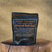 Mineral bath sock packaging labeled 'Desert Midnight' by All Roads on a wooden surface with a blurred background.